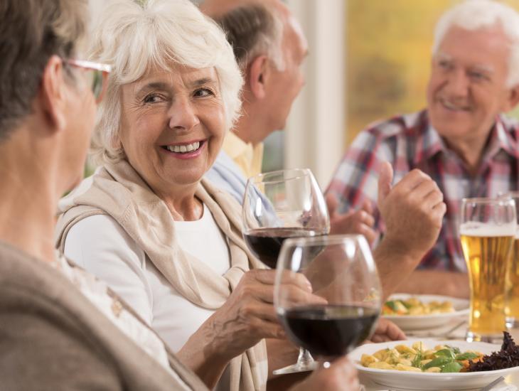 Vier senioren zitten aan het diner met een lekker glaasje erbij.