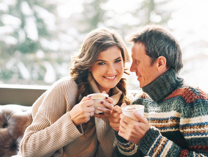 Echtpaar met lekkere warme truien aan drinkt samen koffie op de bank