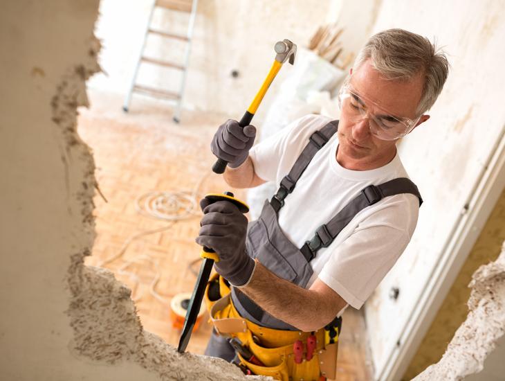 En man van middelbare leeftijd is bezig een muurtje weg te breken met hamer en bijtel.