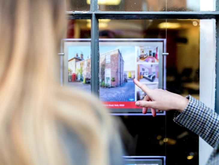 Een stel staat voor de etalage van een makelaar.