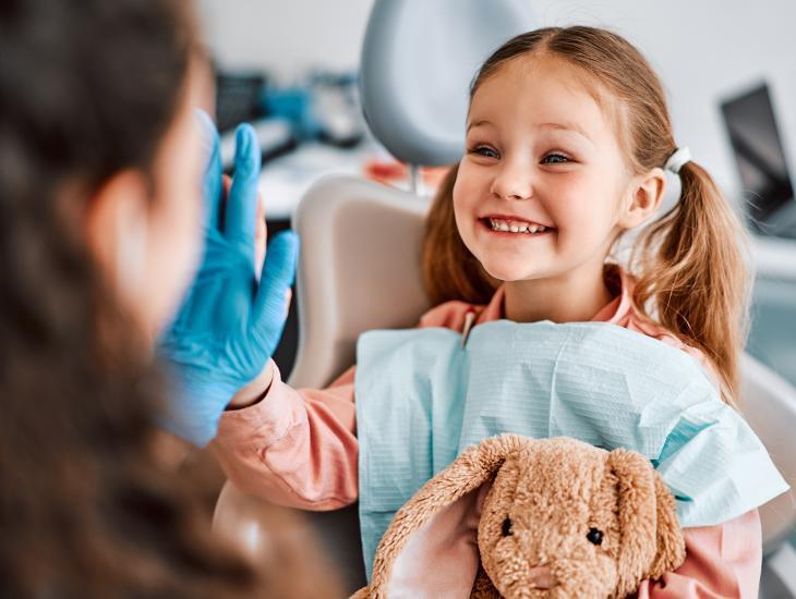 Een klein meisje met een knuffelkonijn in haar hand geeft de dokter een high five.