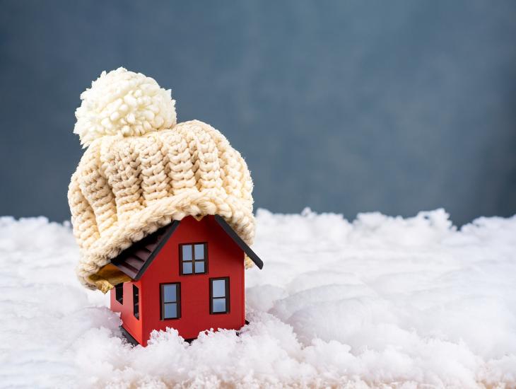 Een miniatuurhuisje in de sneeuw, met een wollen mutsje op