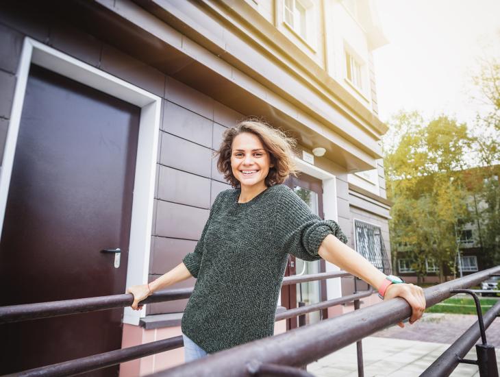 Een jonge, blije vrouw staat op de galerij voor een huis