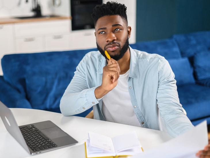 Een man met een brief in zijn hand zit peinzend achter zijn laptop.