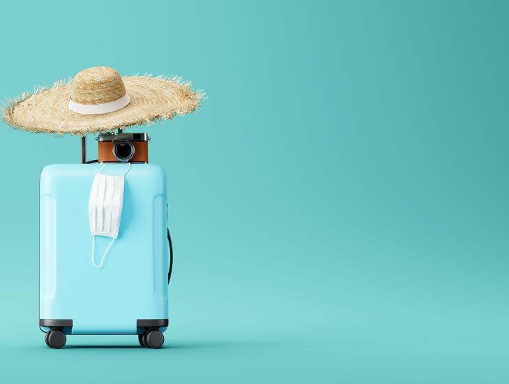 Koffer met daarop een zonnehoed, een fototoestel en een mondkapje