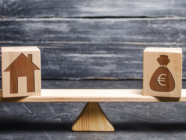 Weegschaal met een huis aan de ene kant en een zak geld aan de andere kant