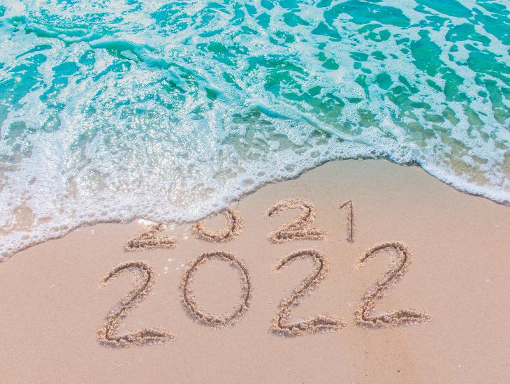 De jaartallen 2021 en 2022, geschreven in het natte zand op de vloedlijn van het strand