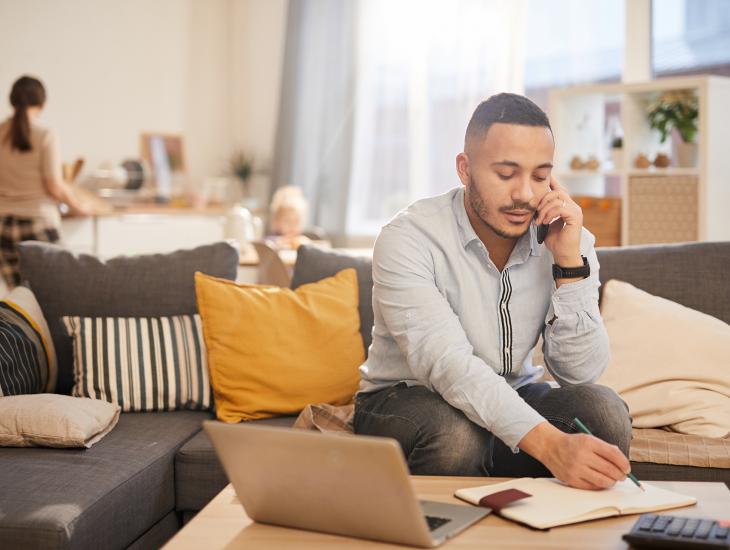 Man zit in de woonkamer achter zijn laptop en rekenmachine en belt zijn financieel adviseur.