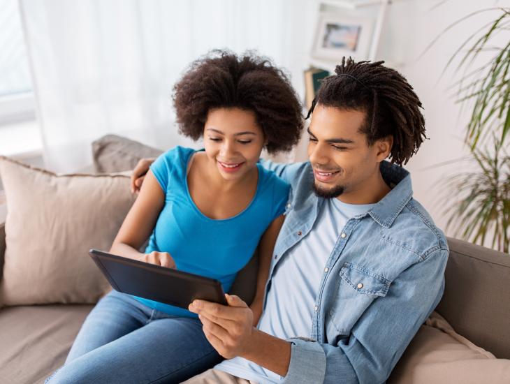 Jong stel zit samen op de bank en bekijkt iets op een iPad