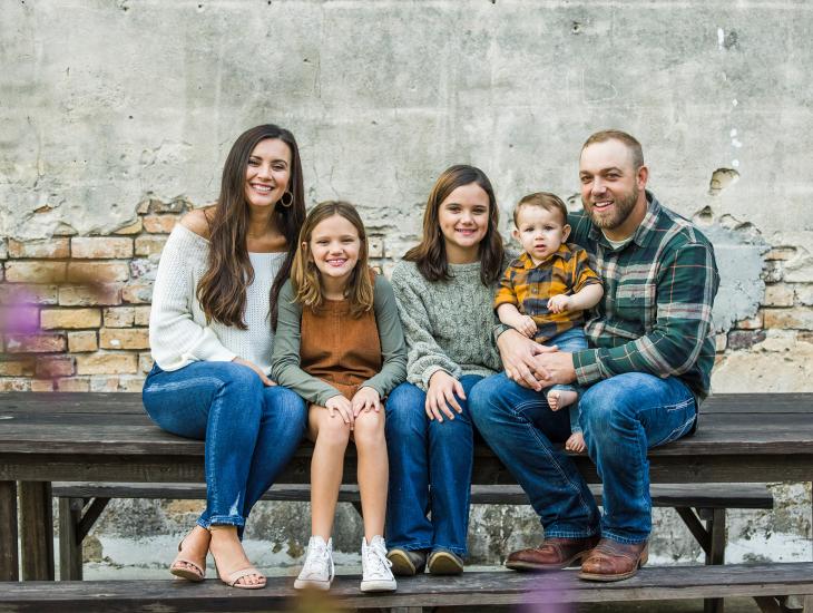 Moeder en vader zitten met drie kinderen op een bankje naast het huis.