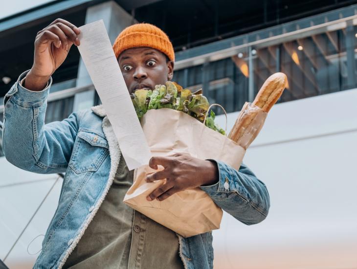 Een man met een tas vol boodschappen staart verbijsterd naar de kassabon.