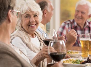 Vier senioren zitten aan het diner met een lekker glaasje erbij.