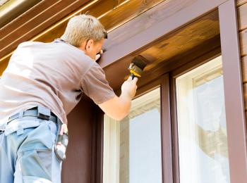 Een man is de kozijnen van zijn huis aan het schilderen