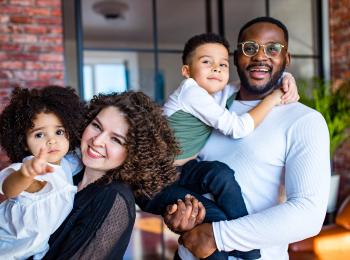 Jong gezin voor hun huis met hun kinderen op de arm