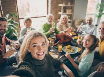 Een vrouw maakt een selfie van drie generaties die aan de eetkamertafel zitten