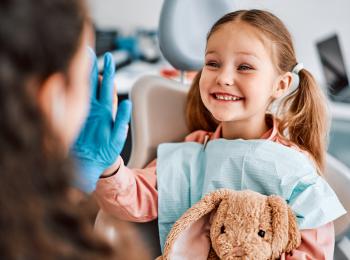 Een klein meisje met een knuffelkonijn in haar hand geeft de dokter een high five.