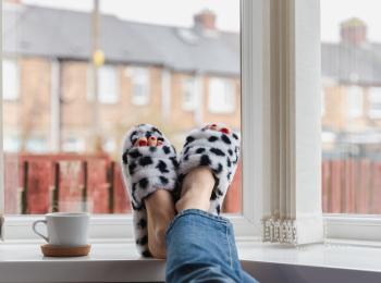 Twee voeten in pantoffels op de vensterbank, op de achtergrond zie je een rijtje huurhuizen.