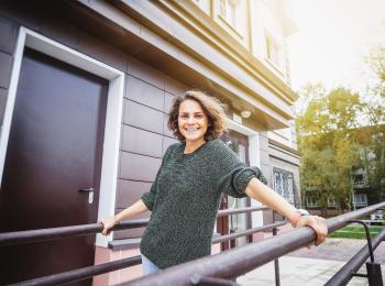 Een jonge, blije vrouw staat op de galerij voor een huis