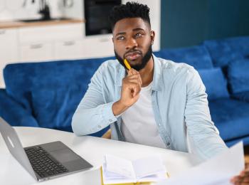 Een man met een brief in zijn hand zit peinzend achter zijn laptop.