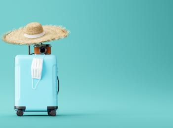 Koffer met daarop een zonnehoed, een fototoestel en een mondkapje