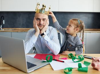Kind zet een kroontje op het hoofd van haar vader, die aan de eettafel aan het werk is