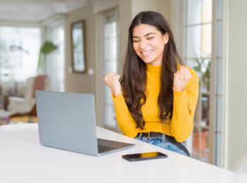 Jonge vrouw zit achter haar laptop en leest iets wat haar blij maakt