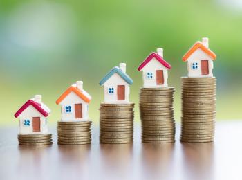 Steeds hogere stapeltjes muntgeld met daar bovenop een huisje