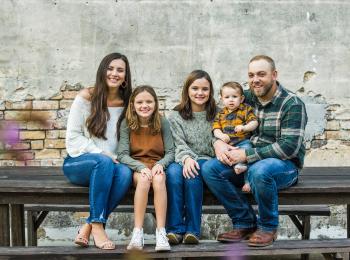 Moeder en vader zitten met drie kinderen op een bankje naast het huis.